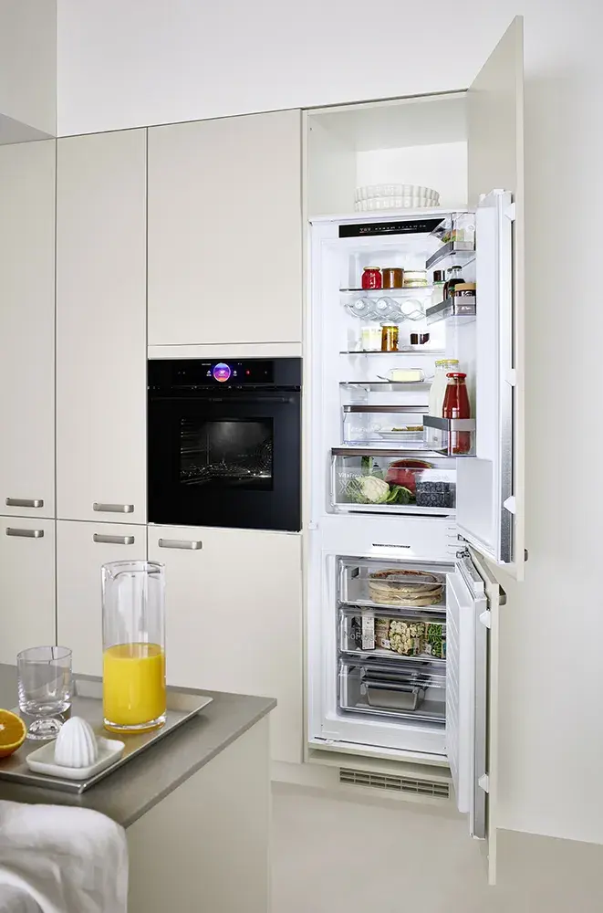 Geöffneter, eingebauter Kühlschrank in moderner Küche, gefüllt mit Lebensmitteln.